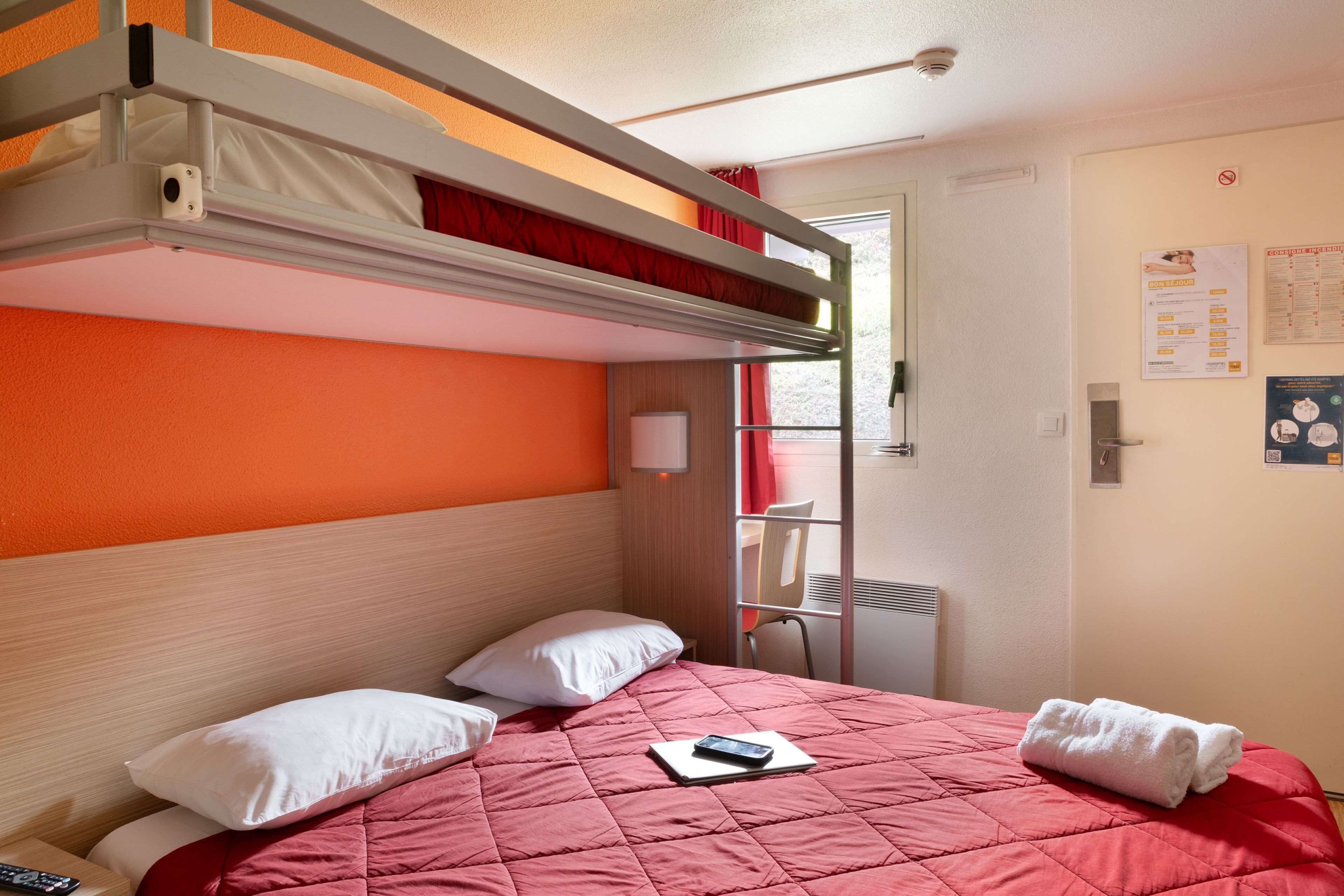 Een stapelbed met een rode dekbedovertrek, witte kussens en een smartphone op de matras.