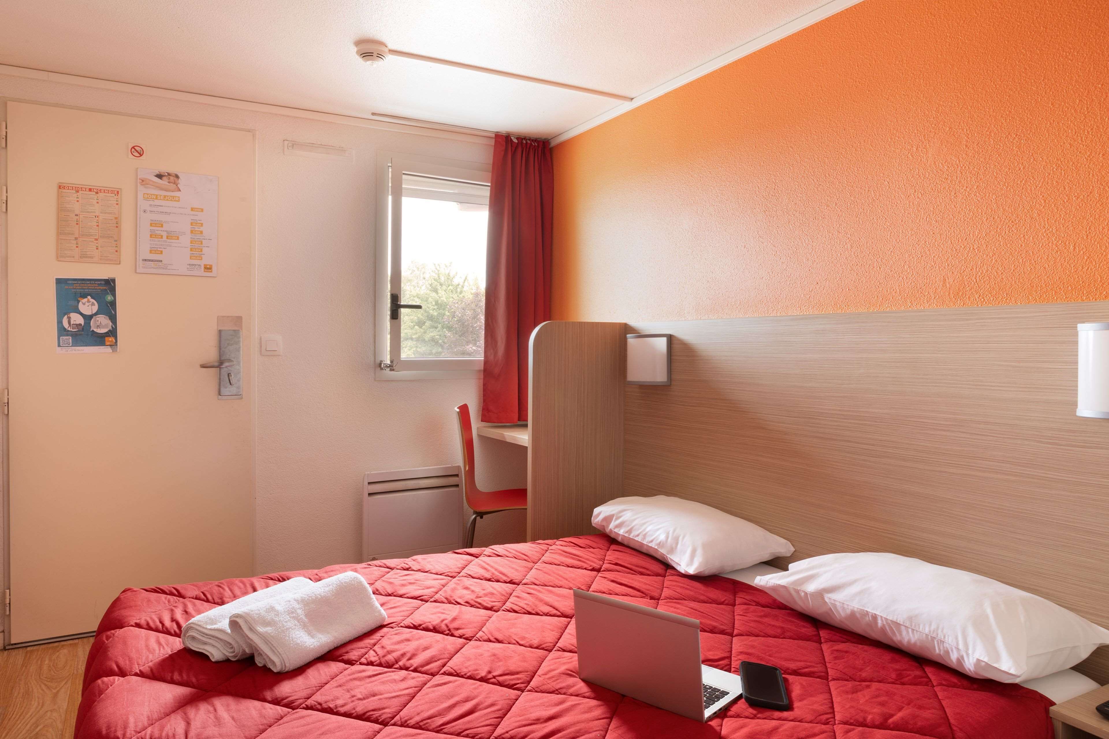 Une chambre d’hôtel avec un lit, un ordinateur portable et un rideau rouge.