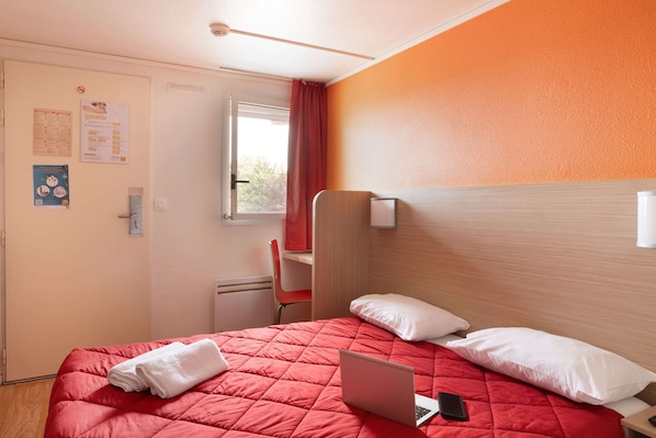 A hotel room with a bed, a laptop, and a red curtain.