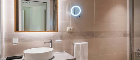 Un baño moderno con un lavamanos redondo, un espejo con luz y una toalla colgada en un perchero.