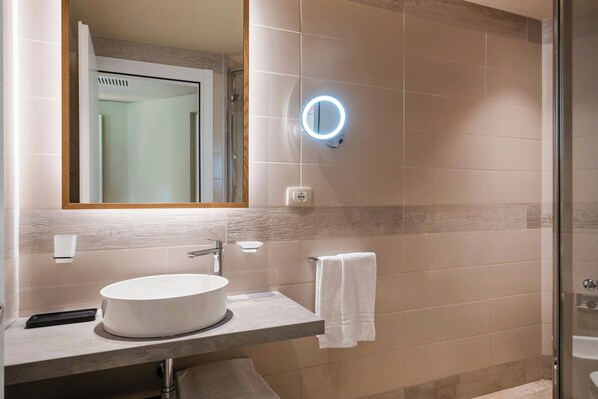 A modern bathroom with a round sink, a mirror with a light, and a towel hanging on a rack.