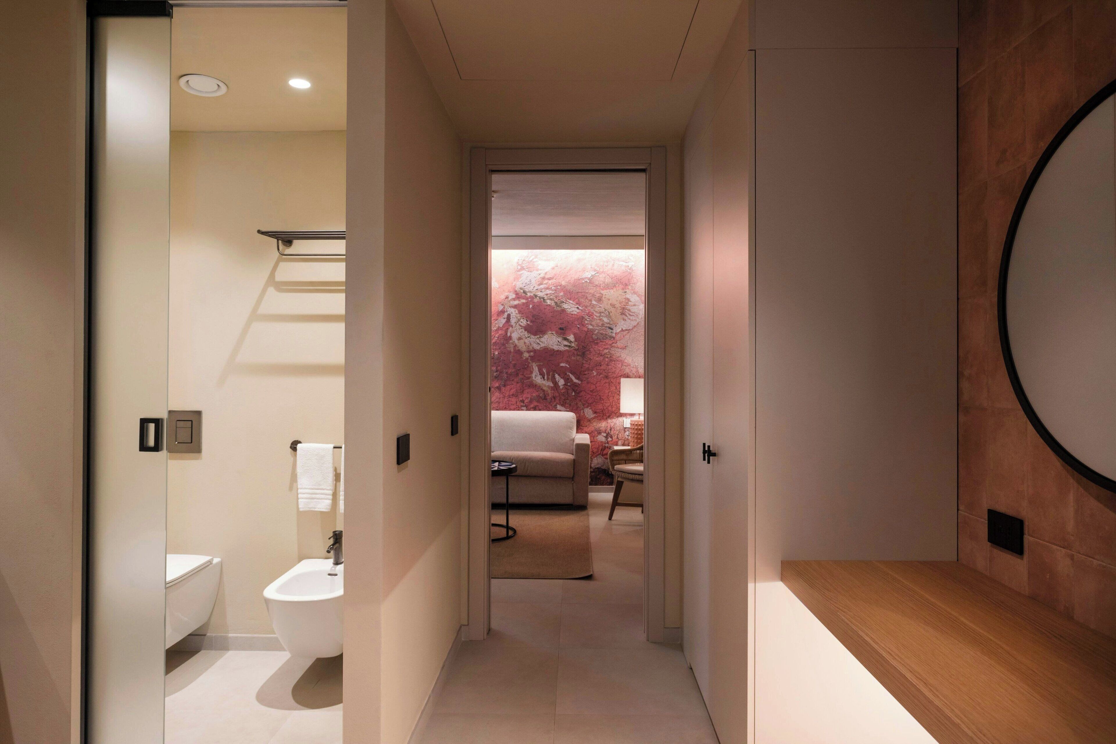 Un baño moderno con inodoro, lavamanos y ducha. Un pasillo conduce a una sala de estar con sofá y mesa de centro.