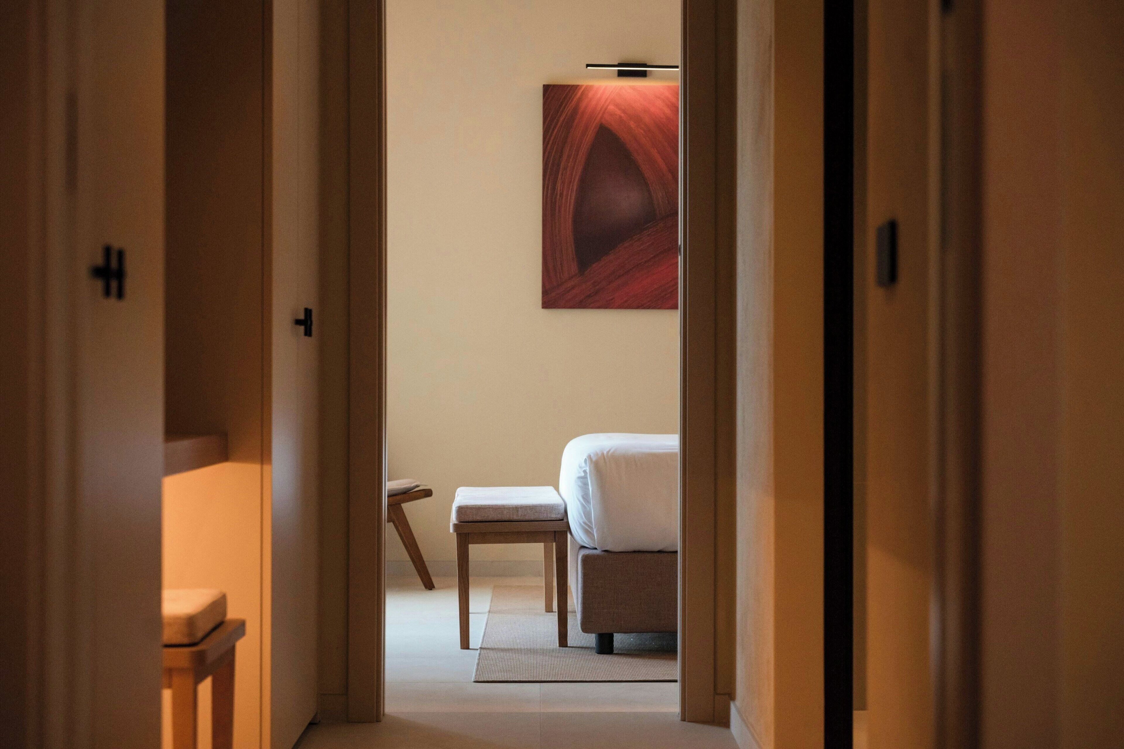 A hotel room with a bed, a small table, and a bench.