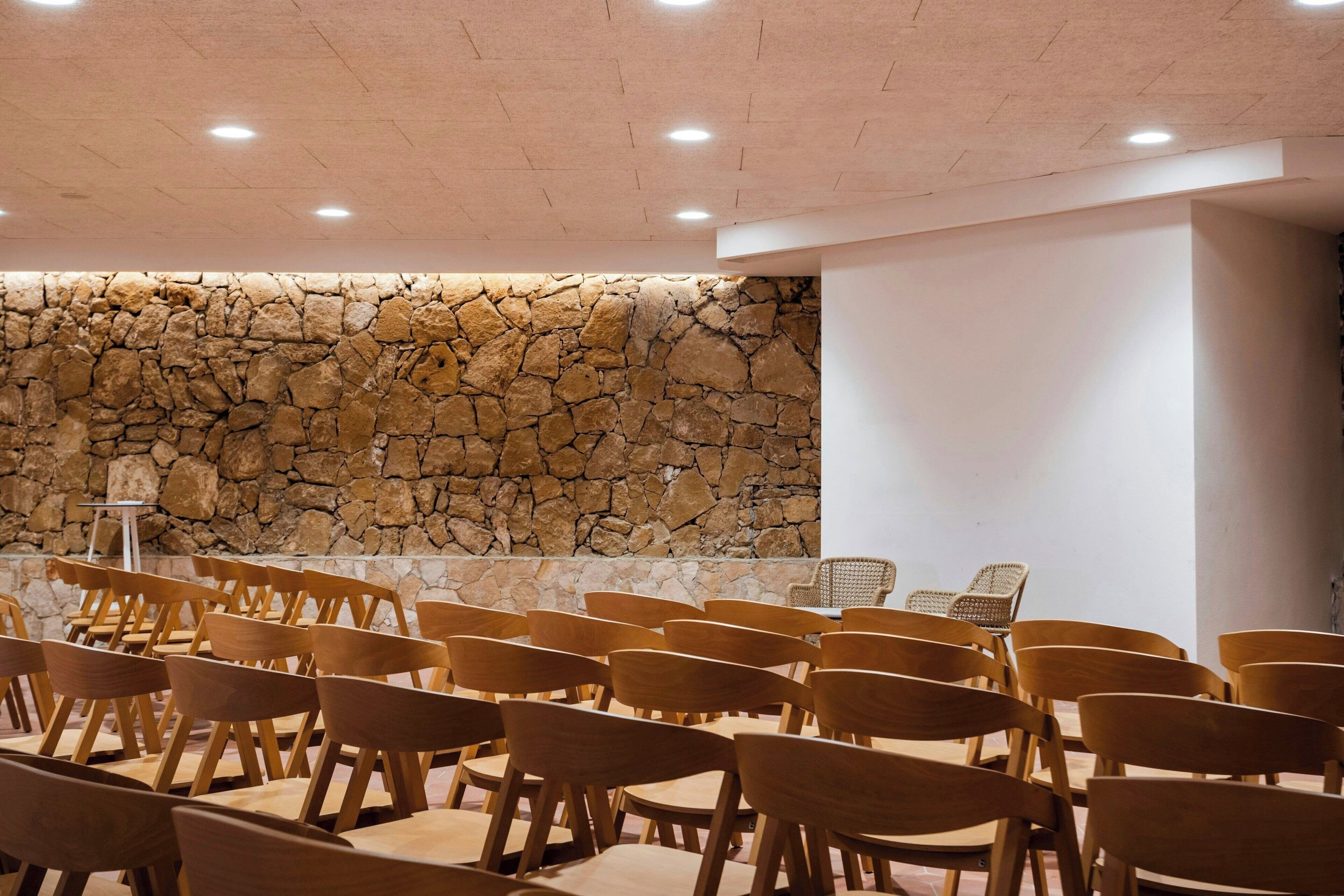 Un salón de conferencias con filas de sillas de madera, una pared de piedra y un atril.