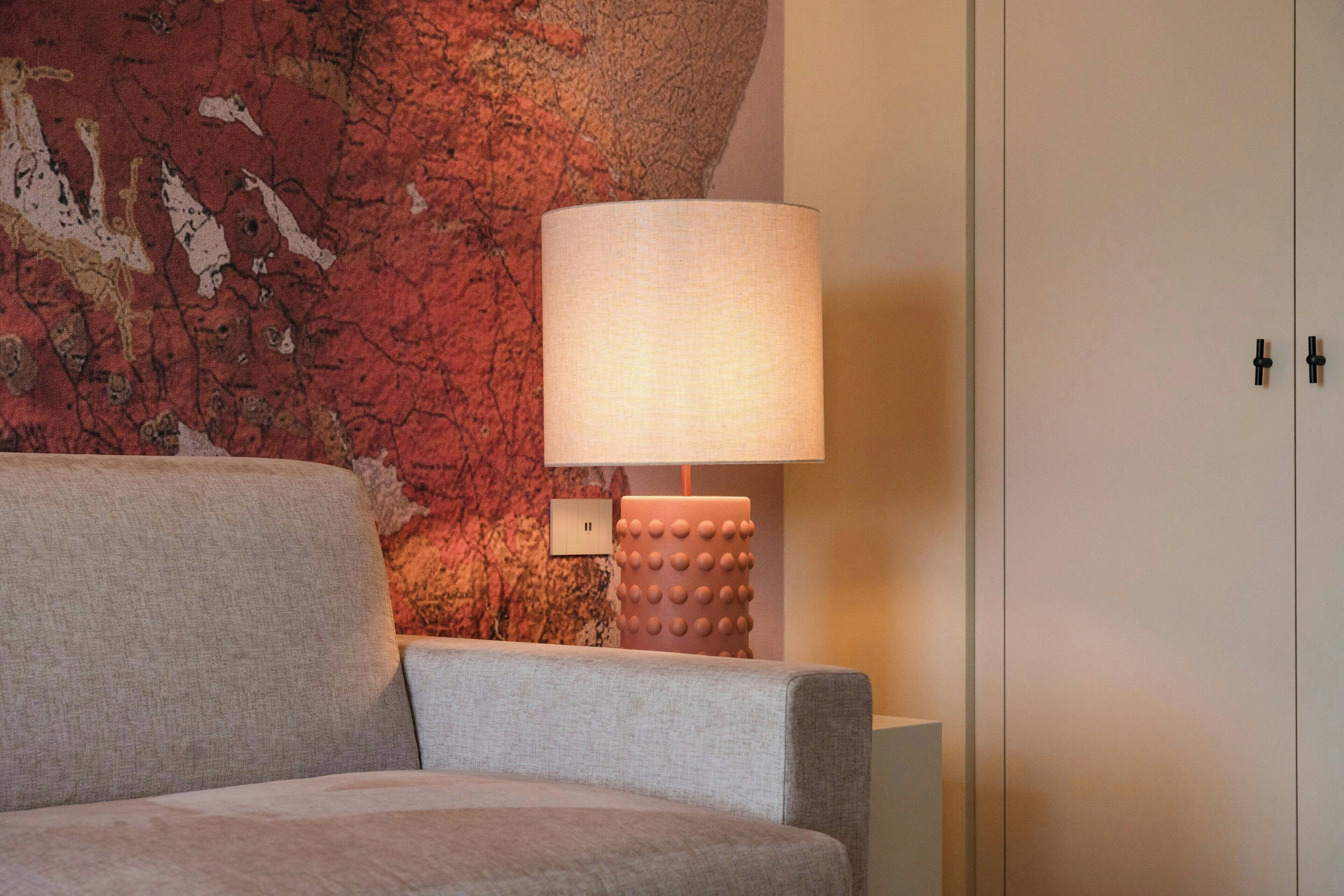 A room with a textured red wall, a grey sofa, a lamp with a textured base, and a white cabinet.