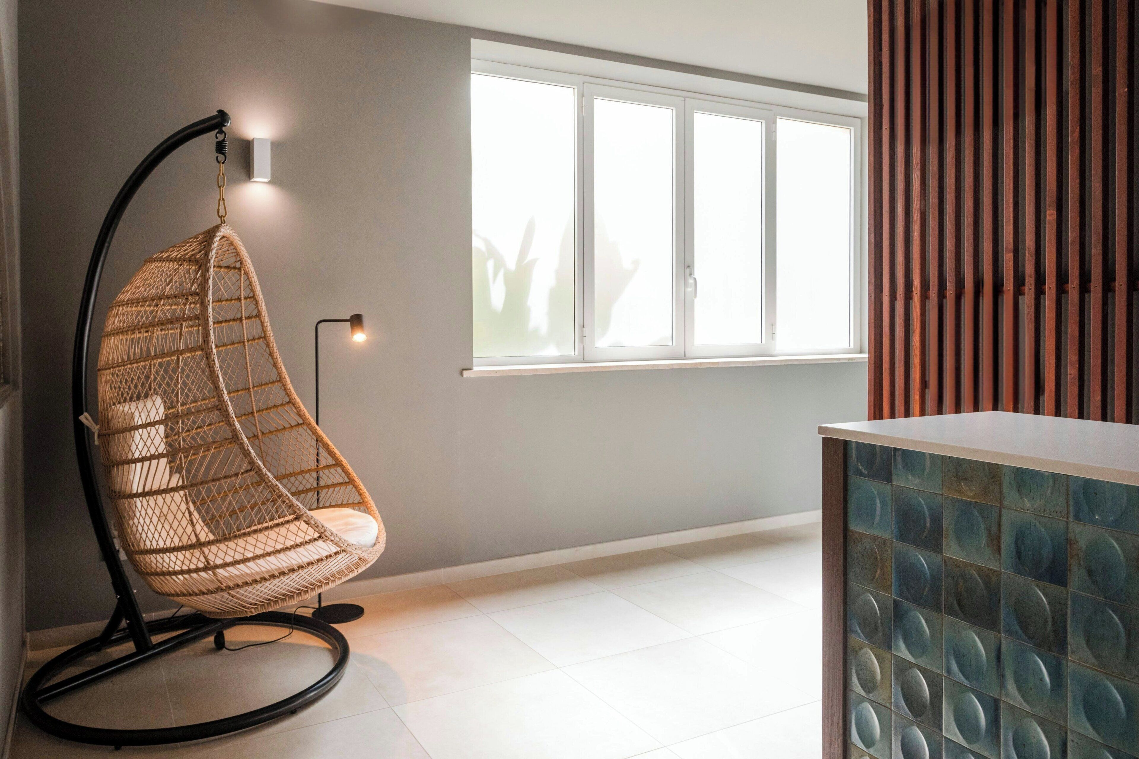 A modern room with a hanging chair, a window with blinds, and a decorative panel.