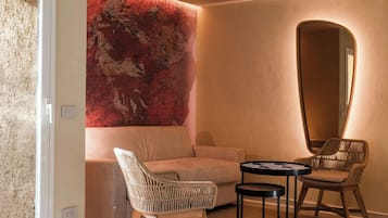 Una camera d'albergo moderna con un letto, un divano, due poltrone in vimini, un tavolino rotondo e un grande specchio.