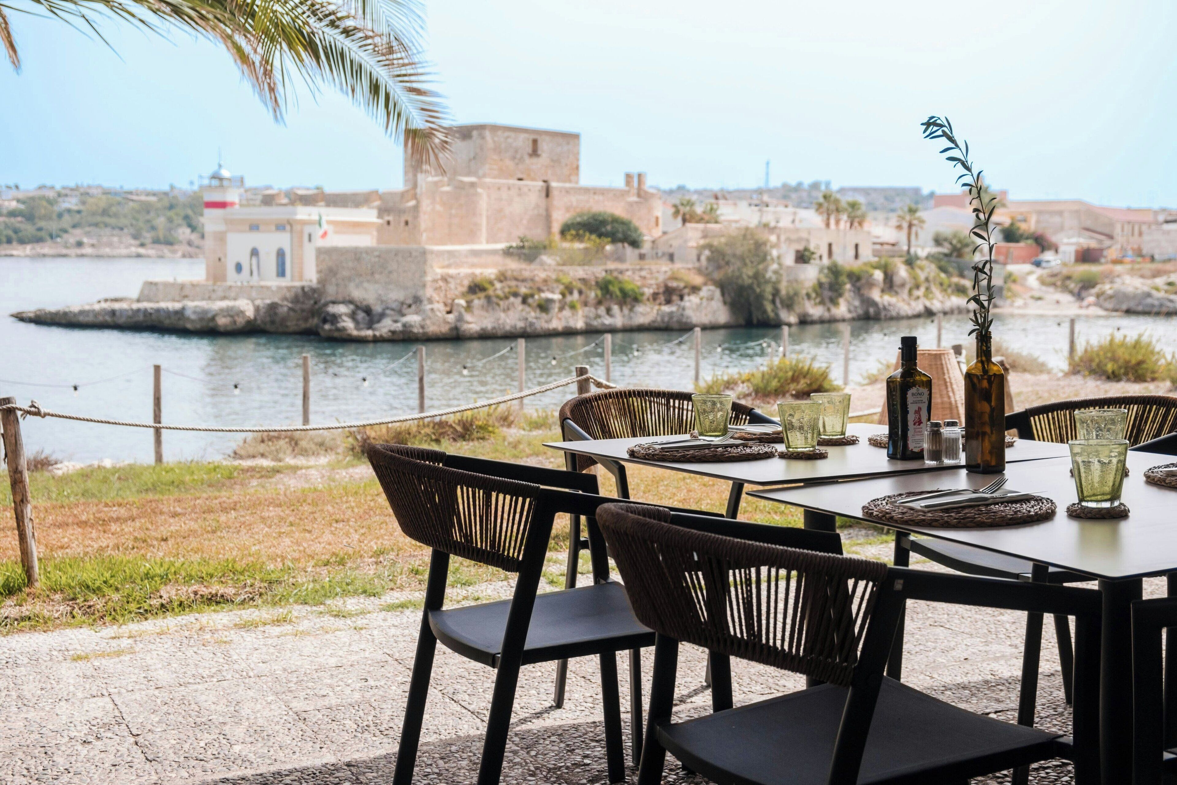 Een terras met eethoek, gedekt voor twee personen, met uitzicht op een waterpartij en een historisch gebouw op de achtergrond.