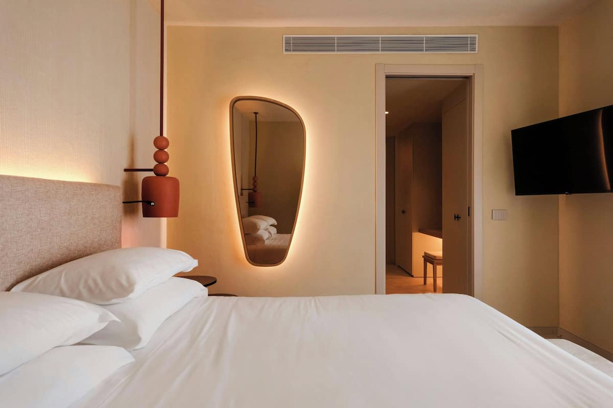 A hotel room with a large bed, a mirror, a television, and a door leading to a bathroom.