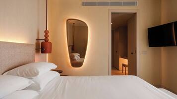 A hotel room with a large bed, a mirror, a television, and a door leading to a bathroom.