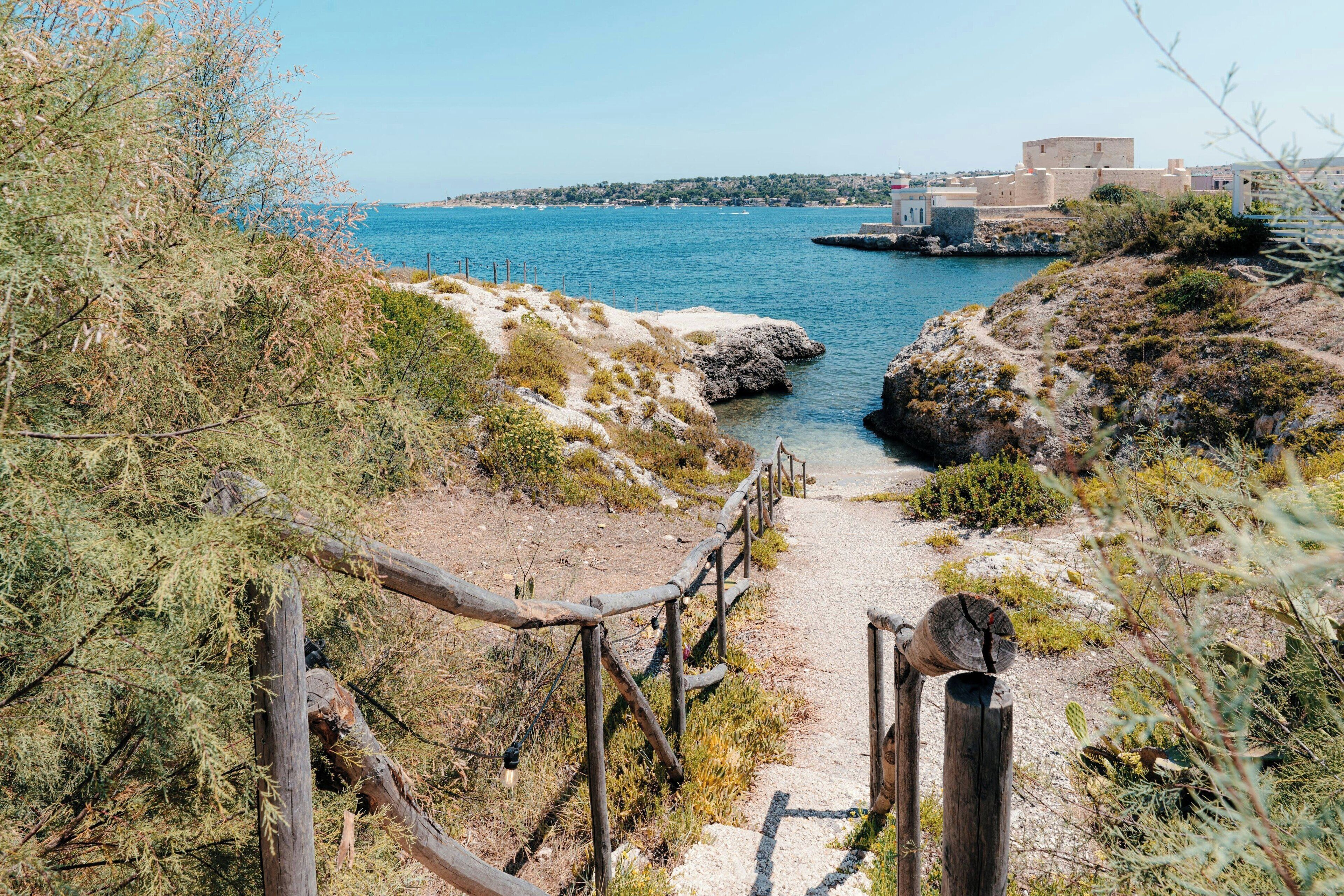 Un sentier côtier menant à un bâtiment fortifié d’où l’on a une vue dégagée sur la mer.