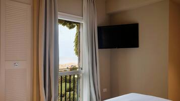 Ein Hotelzimmer mit einem Bett, einem an der Wand befestigten Fernseher und einem Fenster mit Vorhängen.