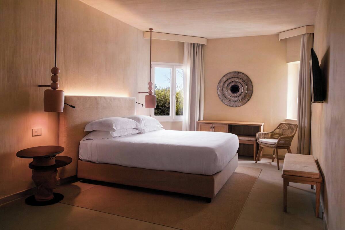 A modern hotel room with a large bed, a desk, a chair, and a wall-mounted TV.
