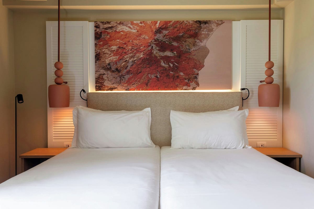 A double bed with white linens, two bedside tables, and a large abstract painting above the bed.