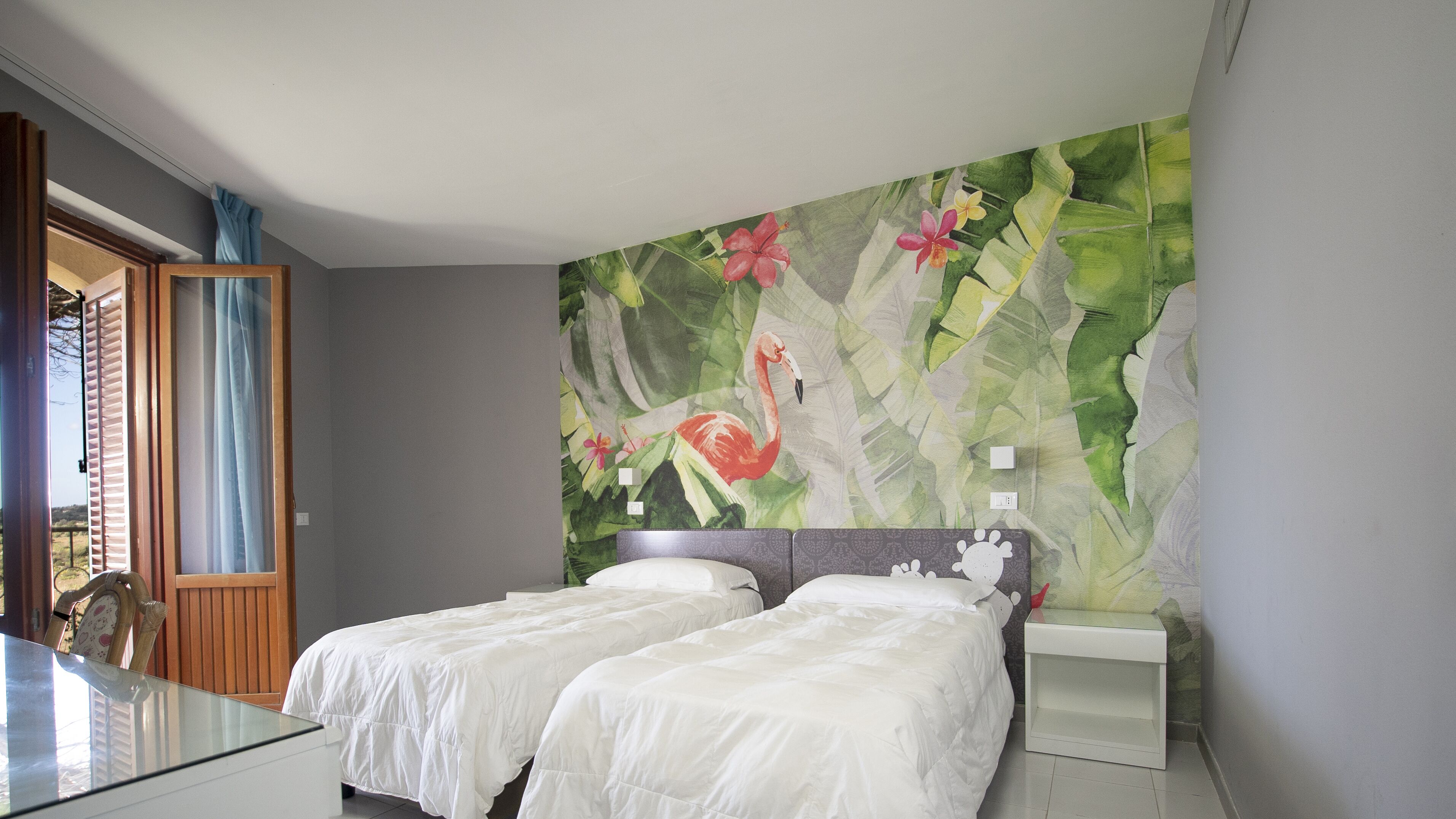 Hotelkamer met twee bedden, een grote bloemmuur en uitzicht op het landschap door een deur.