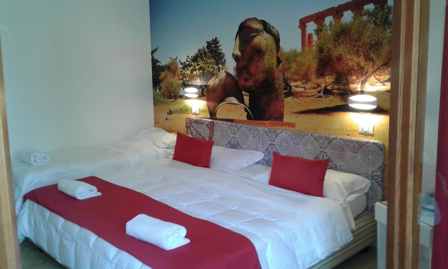 Camera d'albergo con un letto grande, biancheria rossa e bianca, una testiera con motivo decorativo e un affresco raffigurante un cavallo sulla parete.