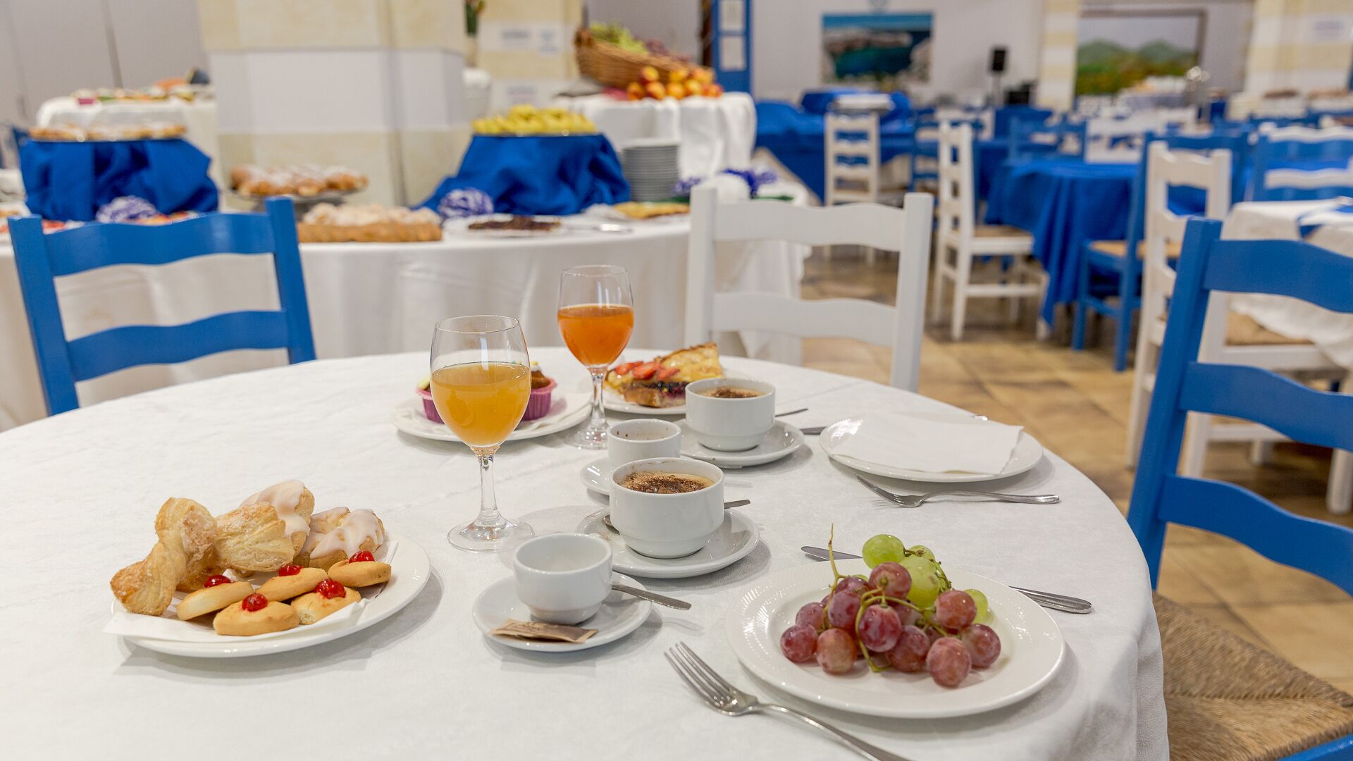 A dining area with round tables set for breakfast, featuring croissants, fruit, and beverages.