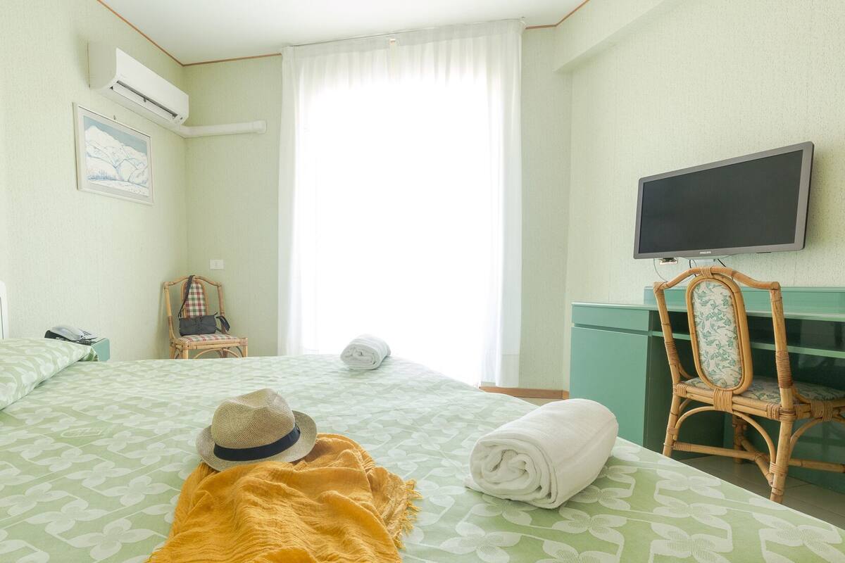 Una habitación de hotel con una cama, televisión, una silla y una ventana con cortinas.