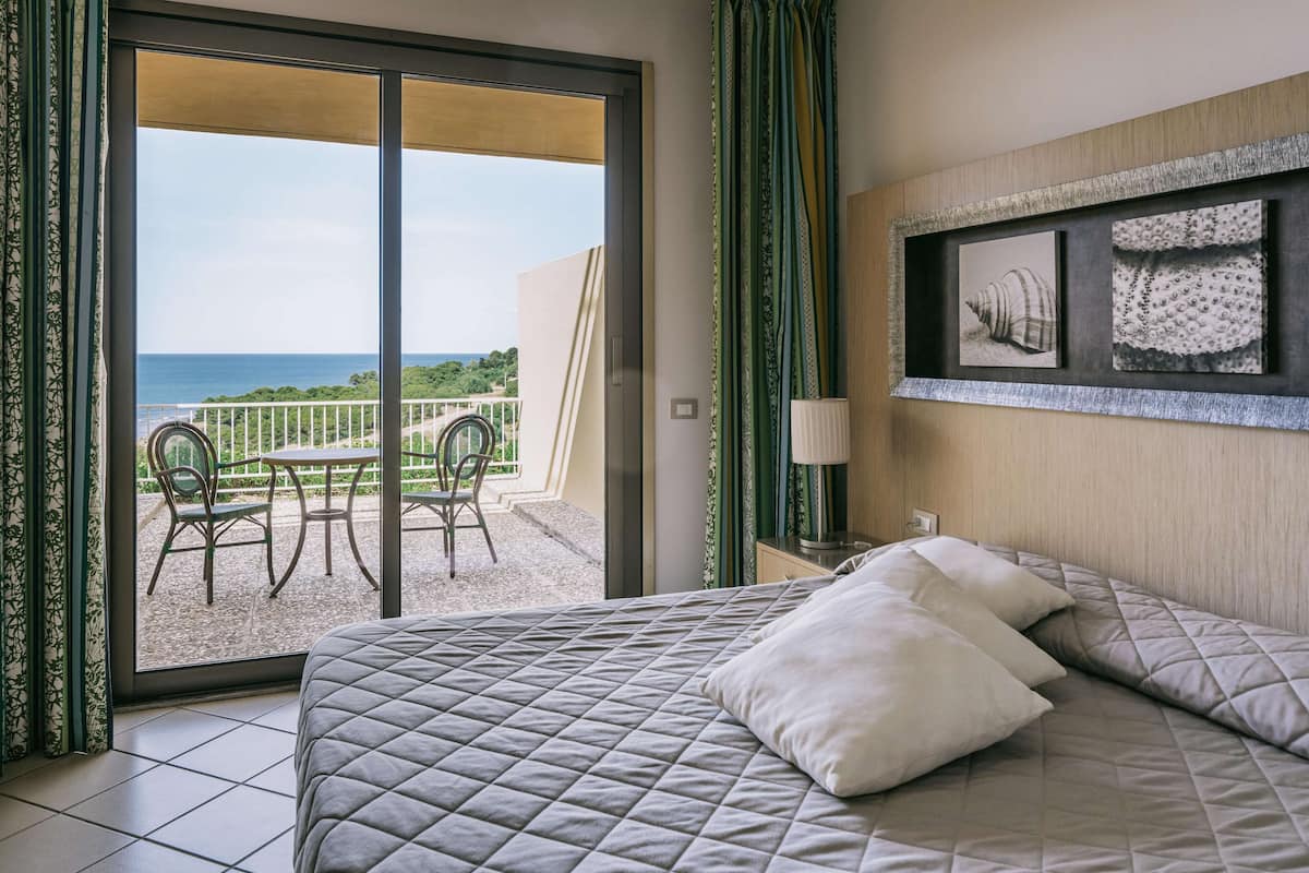 Ein Hotelzimmer mit einem Bett, einem Balkon mit Tisch und Stühlen sowie Bildern an der Wand.