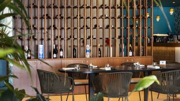 Un restaurante con una larga estantería de madera para vinos, sillas de mimbre negro y una pared azul.