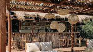 An outdoor seating area with a bar, wicker furniture, and a thatched roof. - Mangia's Torre del Barone Resort and SPA (Sciacca)