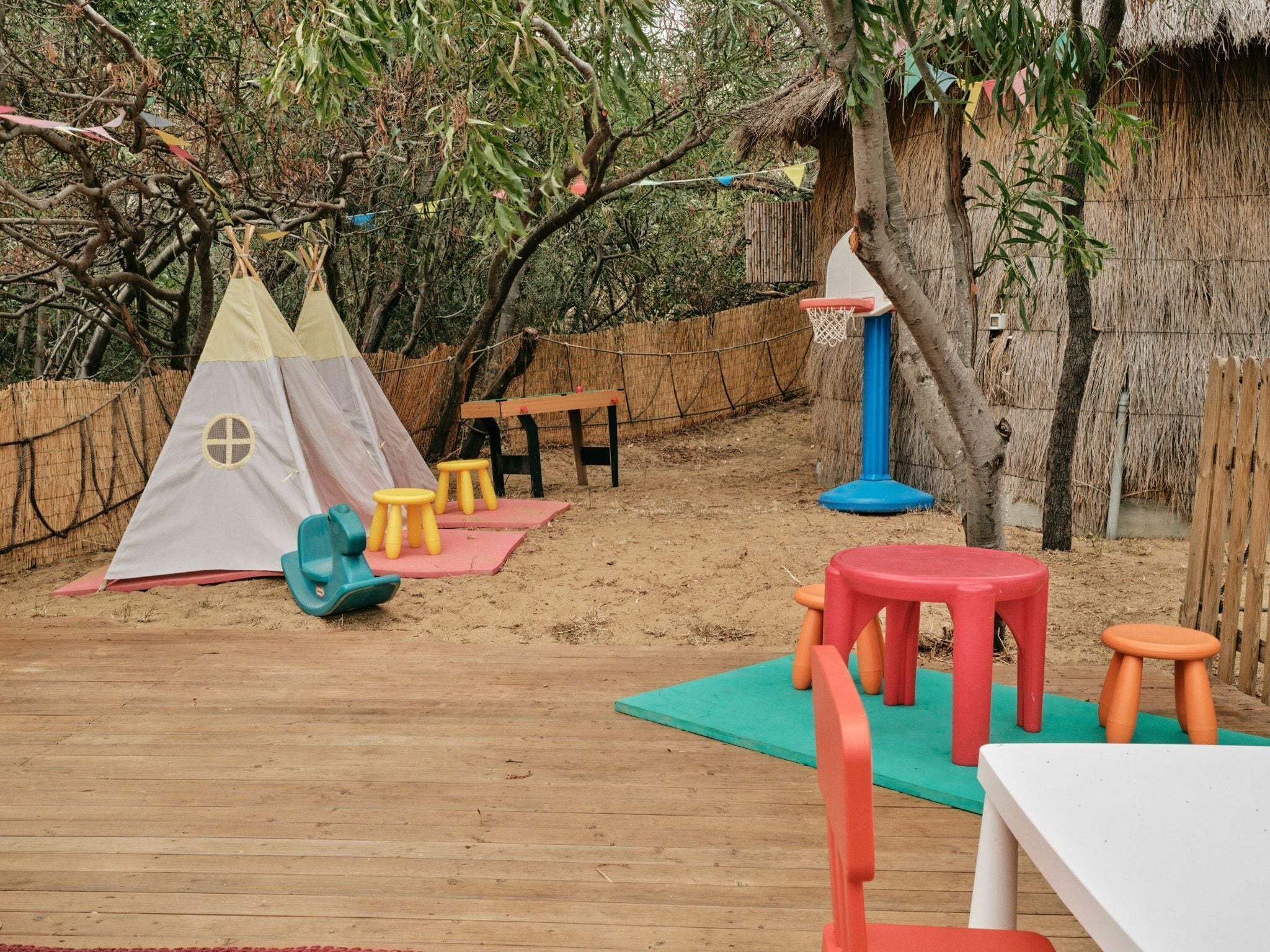 A wooden deck with a play area including a teepee, stools, and a table.