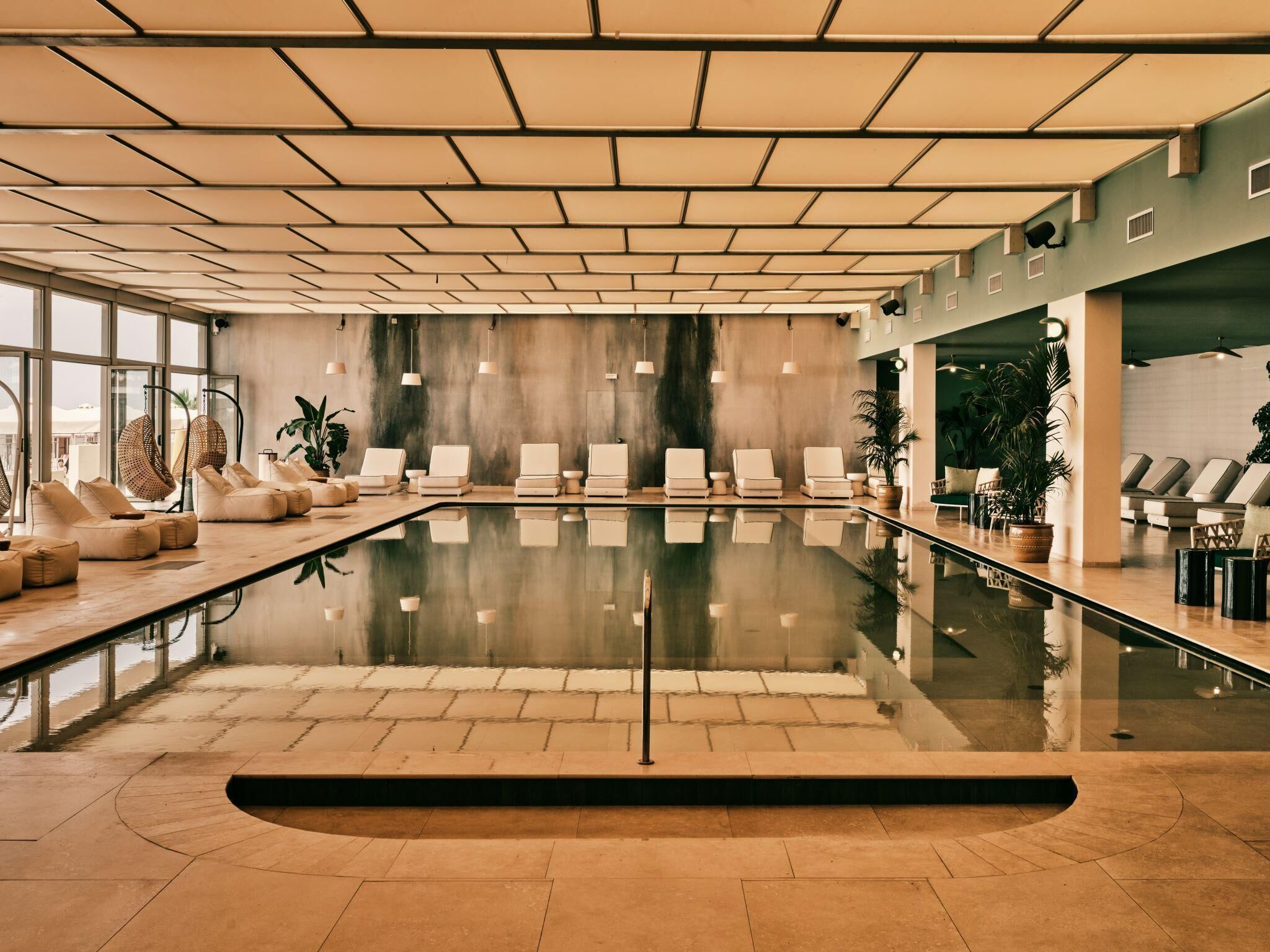 A spacious indoor swimming pool with lounge chairs and a clear view of the outside.