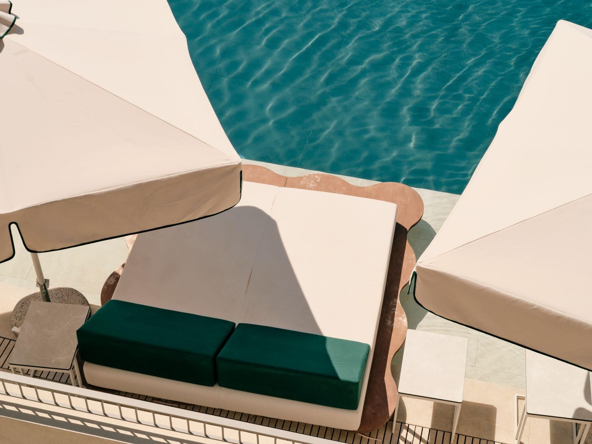 Un área de descanso junto a la piscina con sillas reclinables blancas y un banco acolchado verde.