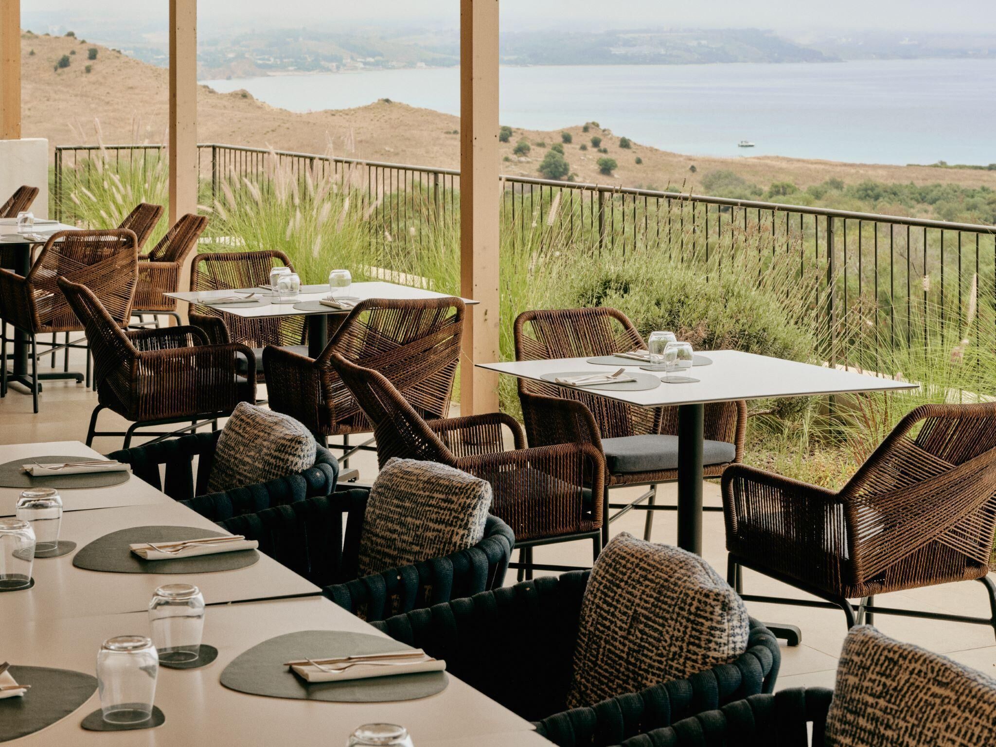 An outdoor dining area with wicker chairs and tables, overlooking a scenic landscape.