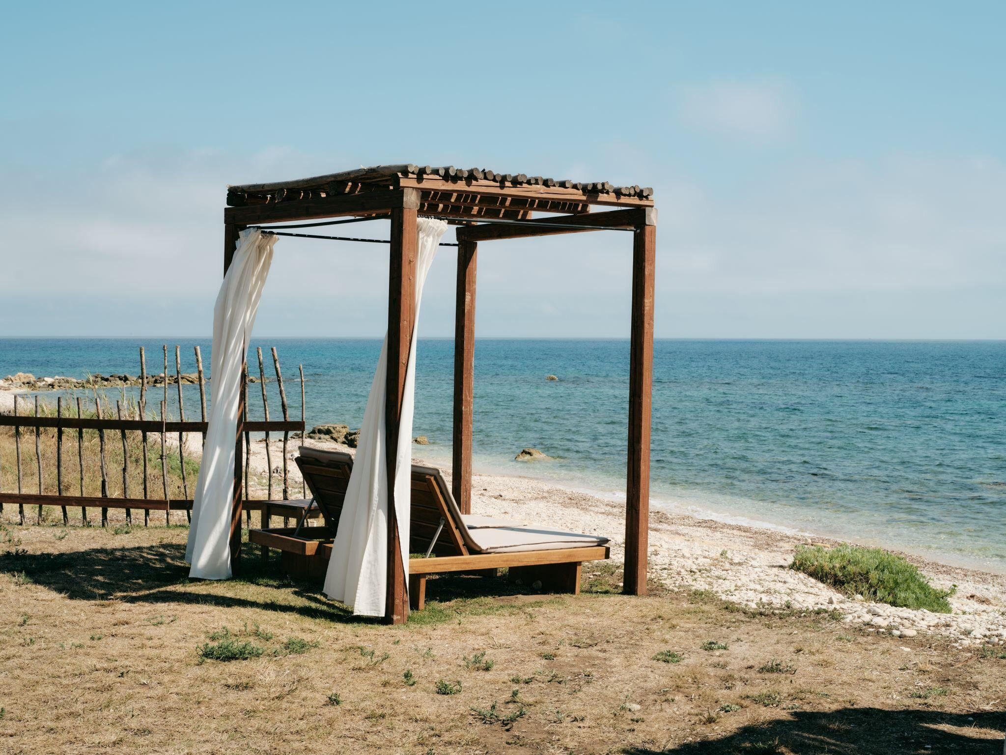 A wooden beach cabana with a canopy, a bench, and a table.