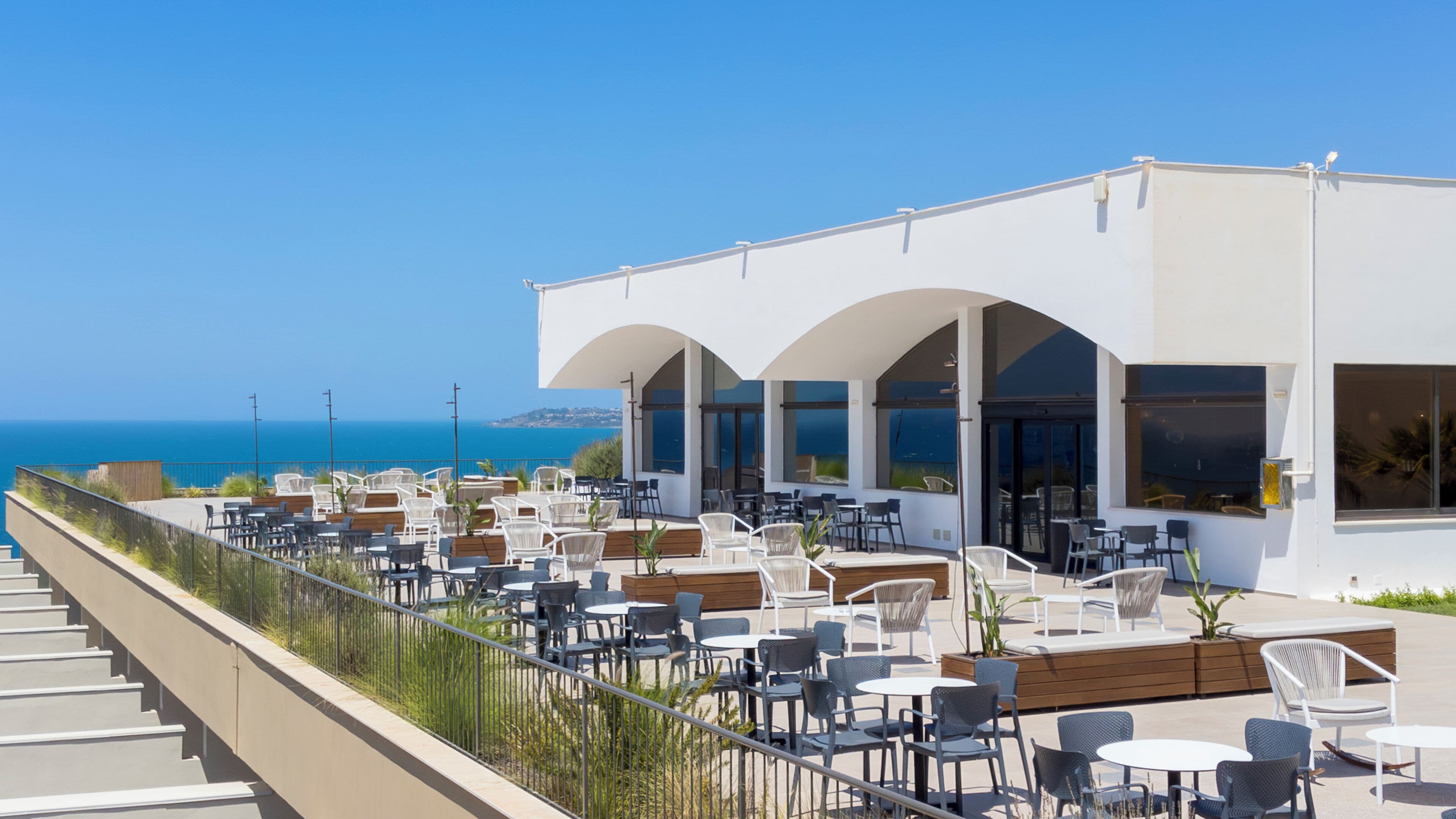 A rooftop terrace with outdoor seating, overlooking a coastal view.