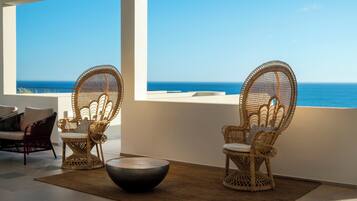 Un balcon avec des fauteuils en osier et une table ronde, donnant sur la mer.