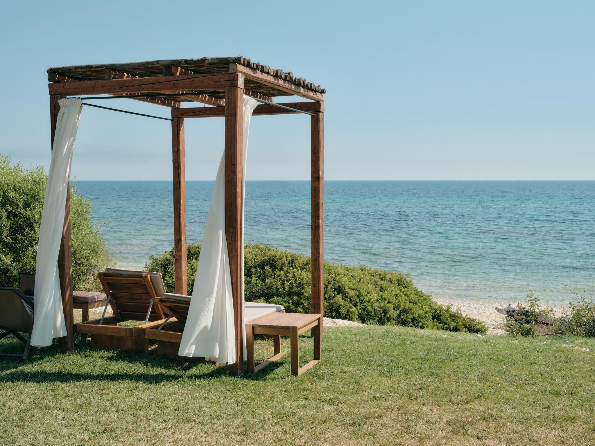 Um gazebo de madeira com um banco e uma mesa, com vista para uma praia.