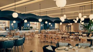 Un restaurante espacioso con varias zonas de comedor, que incluyen mesas redondas y cabinas, además de un bar con mostrador.