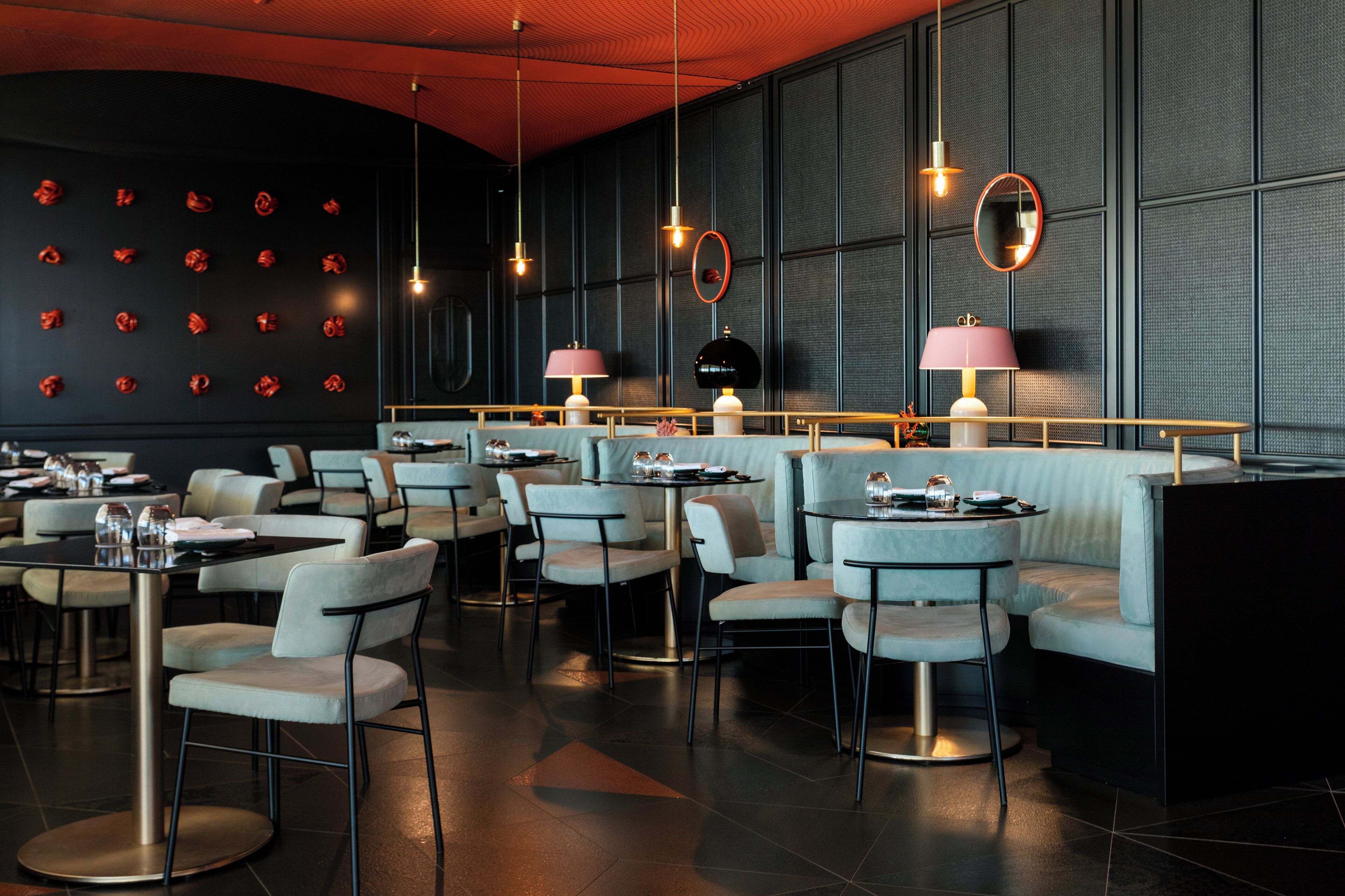A modern restaurant with round tables, cushioned seating, and pendant lighting.