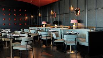 Un restaurant moderne avec des tables rondes, des sièges rembourrés et des luminaires suspendus.