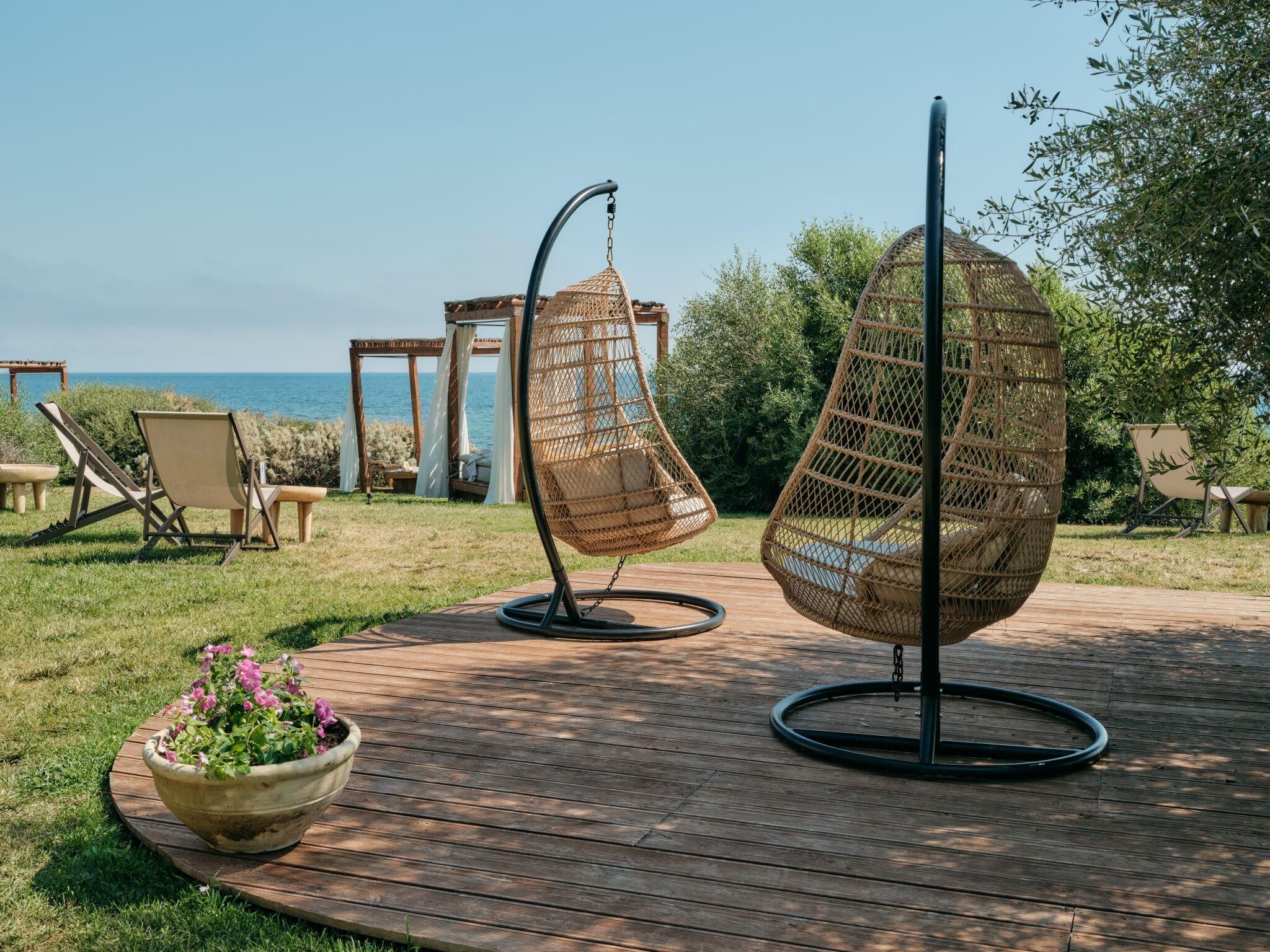 Una terraza de madera con dos sillones colgantes de mimbre y una planta en maceta.
