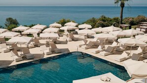 A poolside area with multiple lounge chairs and umbrellas, overlooking a clear blue sea. - Mangia's Torre del Barone Resort and SPA (Sciacca)