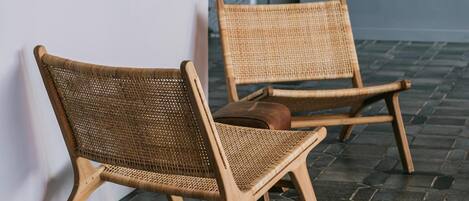 Two wicker chairs against a wall with framed black and white artwork, a stone wall, and a tiled floor.