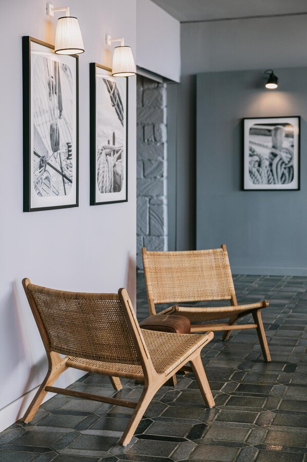 Two wicker chairs against a wall with framed black and white artwork, a stone wall, and a tiled floor. - Mangia's Torre del Barone Resort and SPA (Sciacca)
