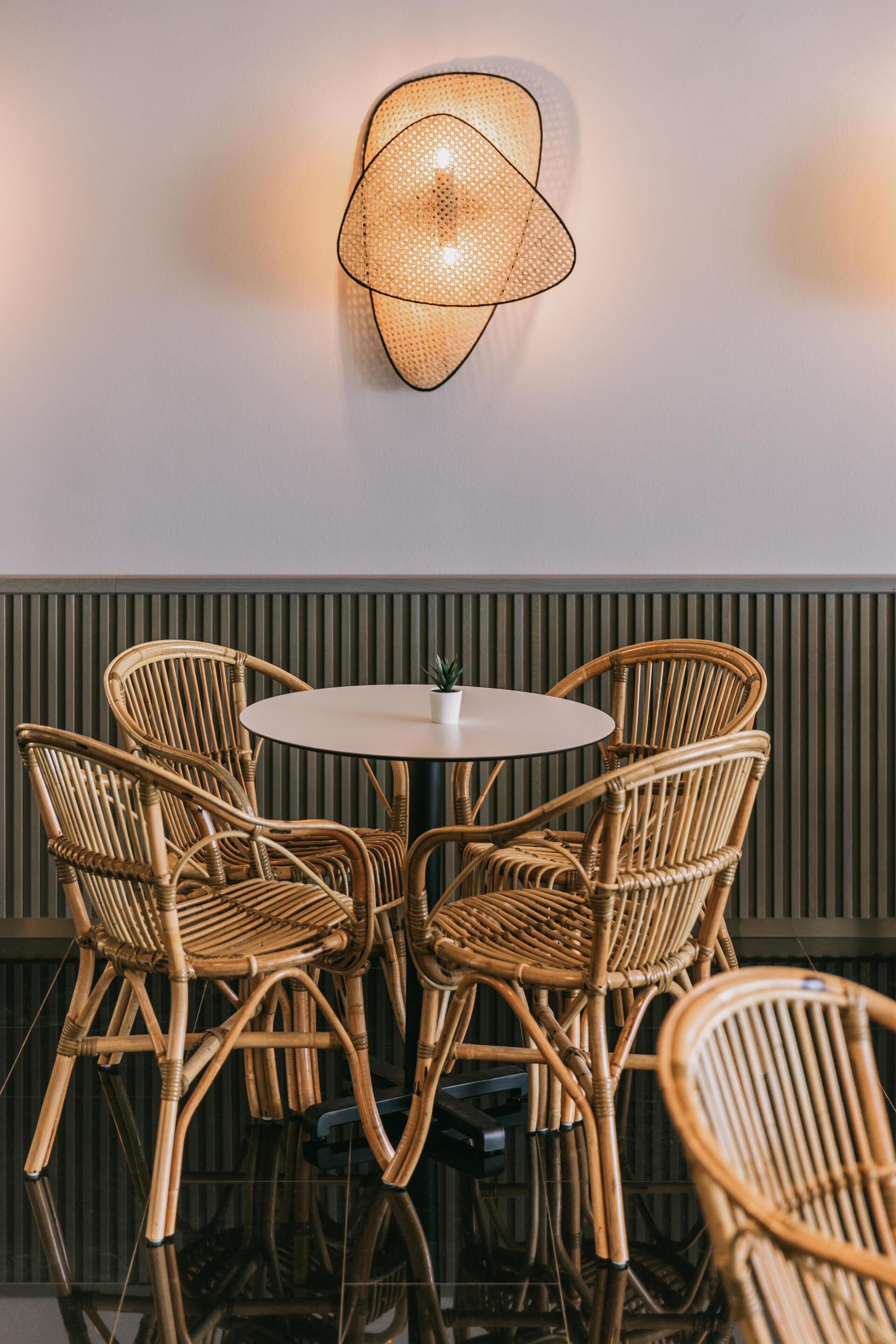 Een ronde tafel met zes rieten stoelen, een wandlamp en een paneel met strepen.