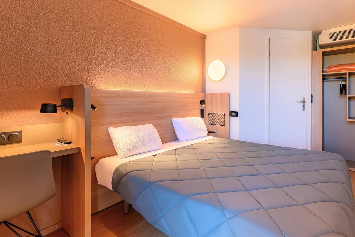 Un dormitorio con cama, mesita de noche, lámpara y armario.
