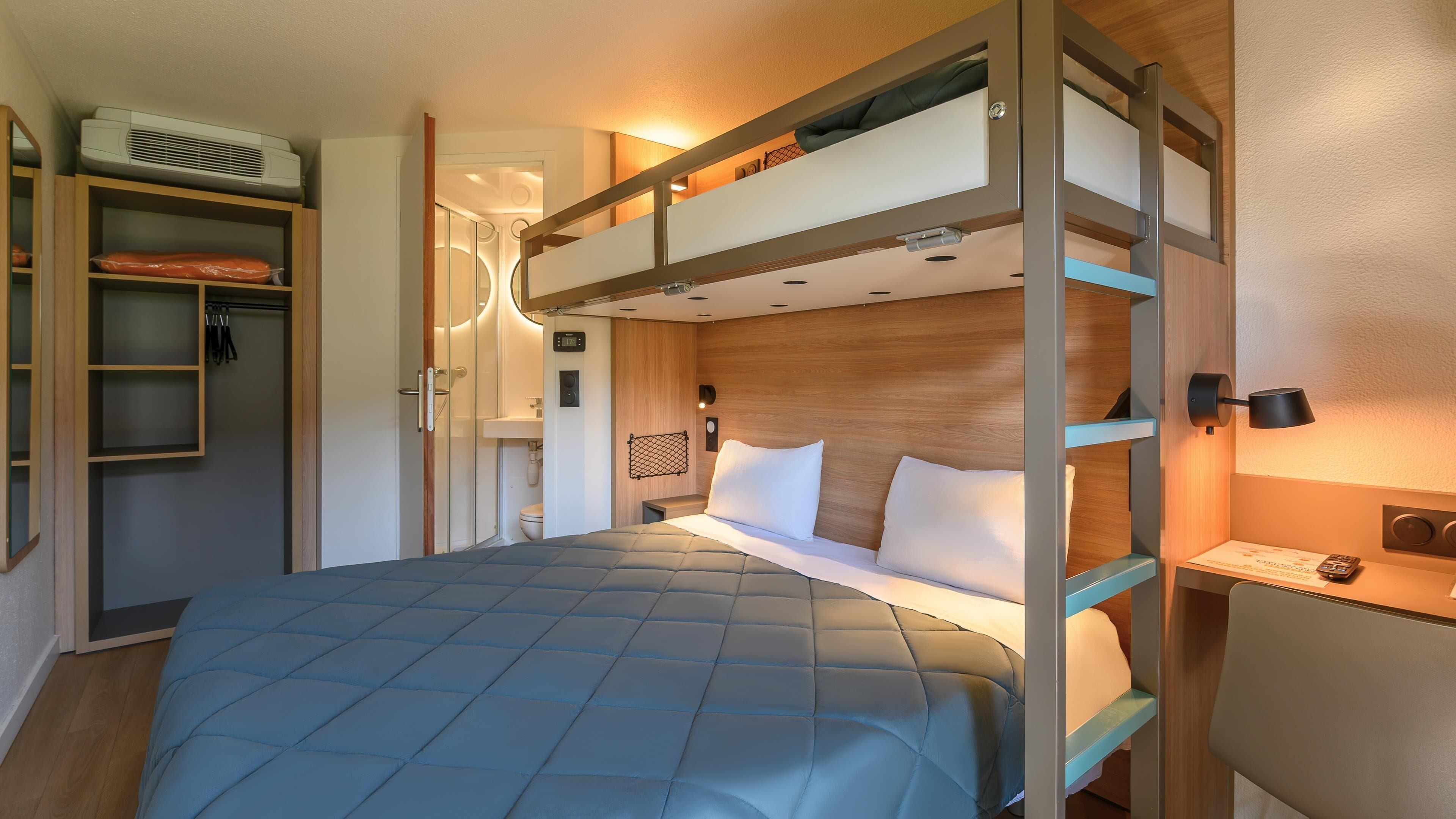 A bunk bed with a headboard, a bedside table, a wall-mounted lamp, and a wardrobe with a mirror.