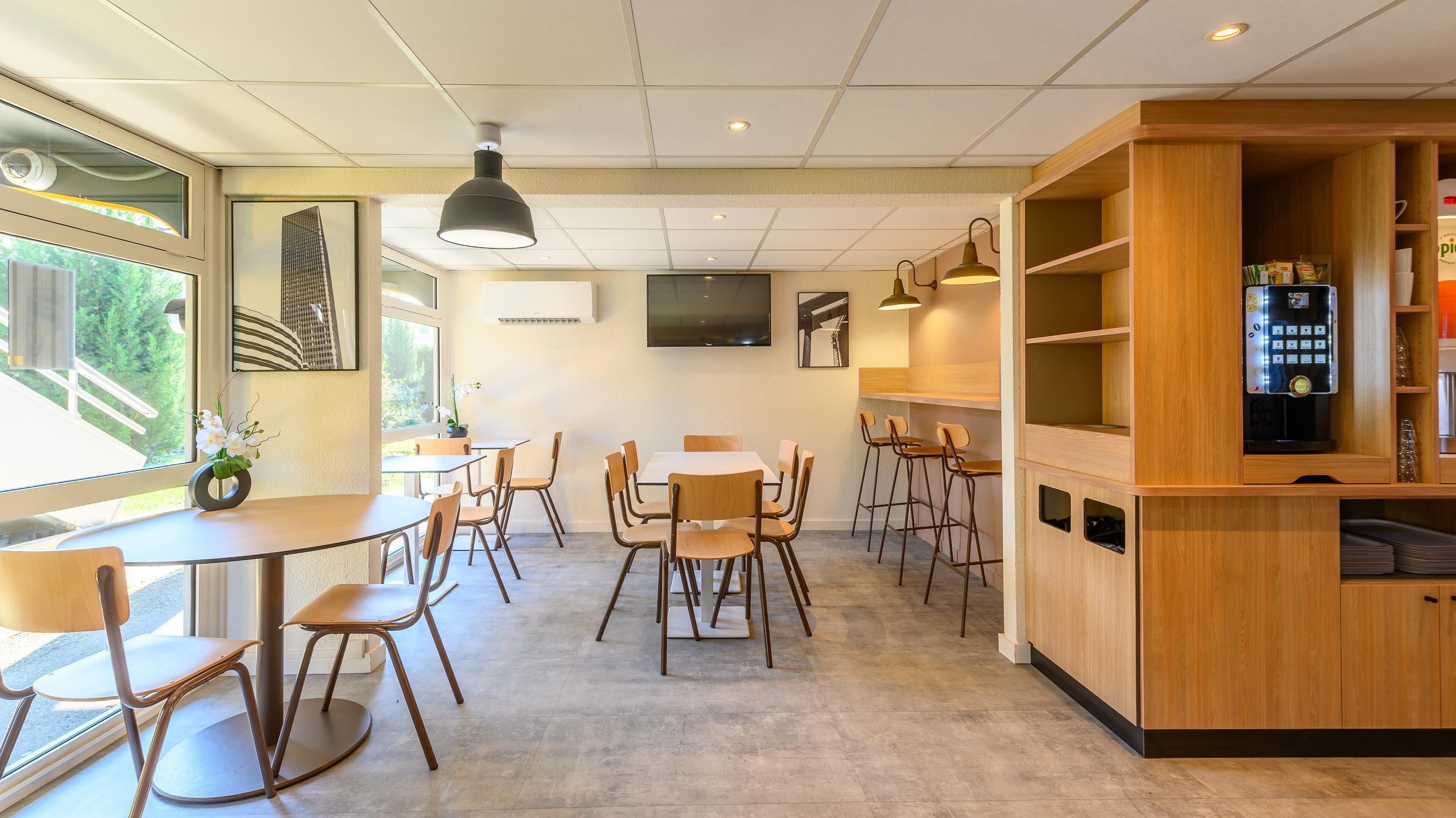 Ein modernes Café mit einer langen Theke, mehreren Tischen und Stühlen.