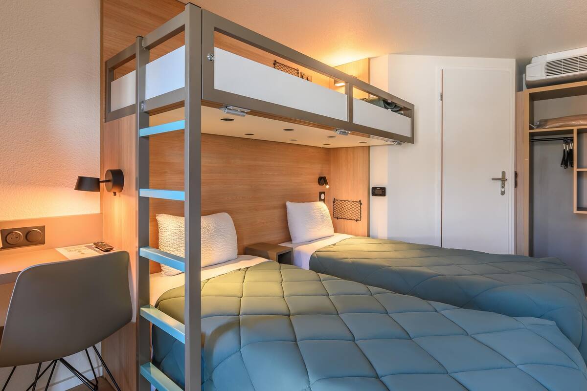 Una habitación de hotel pequeña con una cama individual superpuesta, un escritorio y un armario.