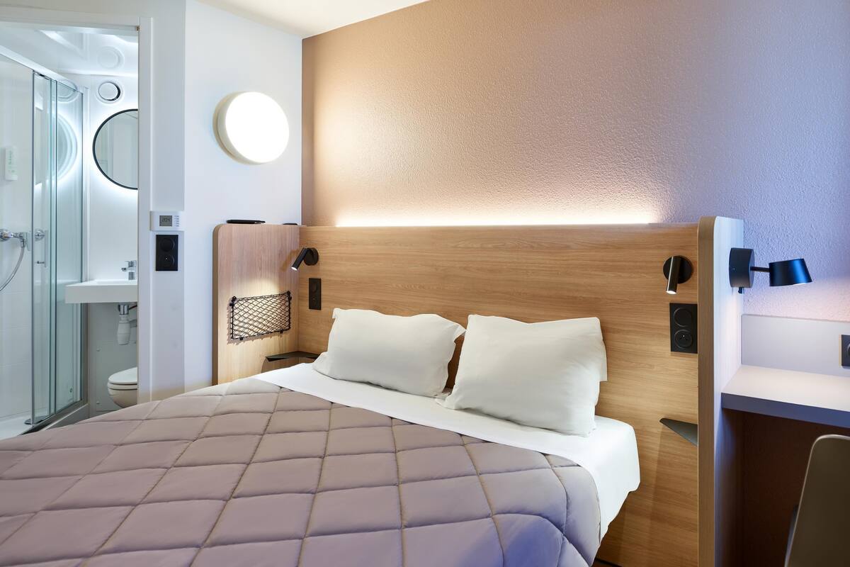 Une chambre d’hôtel comprenant un lit, une table de chevet, une lampe et un espace douche.