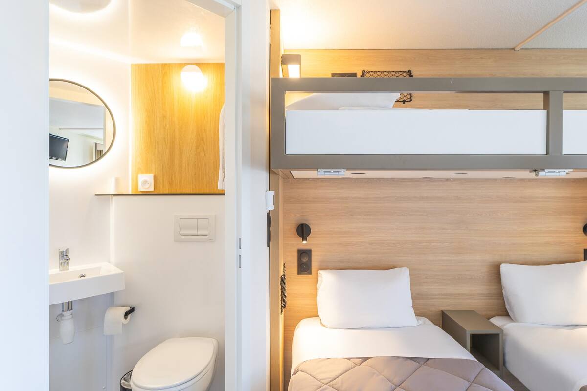 Une chambre d’hôtel compacte comprenant un lit superposé, une petite table de chevet, un miroir et des toilettes.
