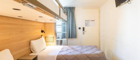 A hotel room with two beds, wooden headboard, ceiling lights, a TV, and a window with curtains.