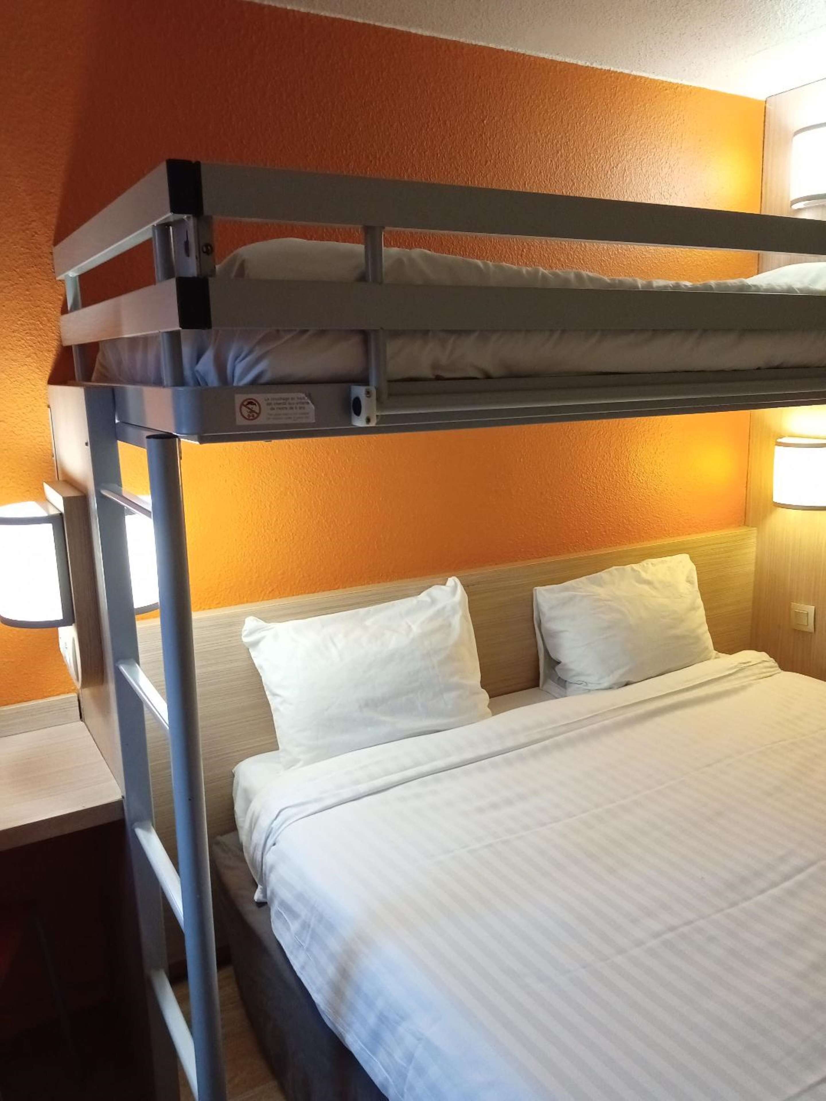A bunk bed with a headboard, white bedding, and a nightstand with a lamp.