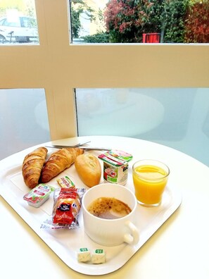 A breakfast tray with croissants, bread, yogurt, juice, and coffee on a white plate. - Premiere Classe Saint Brice Sous Forêt (Saint-Brice-sous-Foret)
